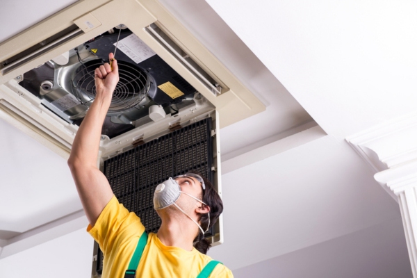 HVAC technician doing a visual inspection of air conditioning unit in the ceiling