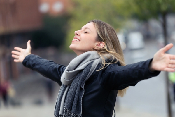 Shot of smiling young woman breathing fresh air and raising arms in the city