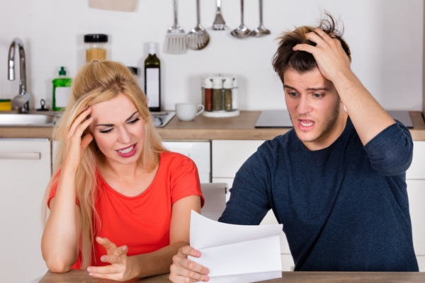 couple looking shocked and stressed while looking at energy bill depicting leaky HVAC air ducts