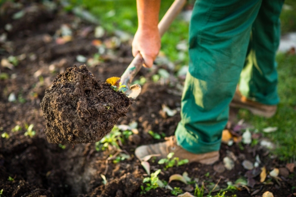 man digging garden soil for landscaping around propane tank