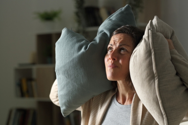 woman covering both ears with pillows due to unusual HVAC ductwork noise