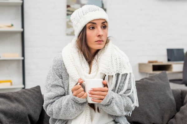 woman staying warm indoors with winter clothes and a cup of tea