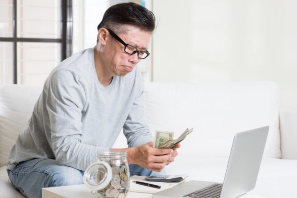 man counting money in front of his laptop with a jar of coins on the side