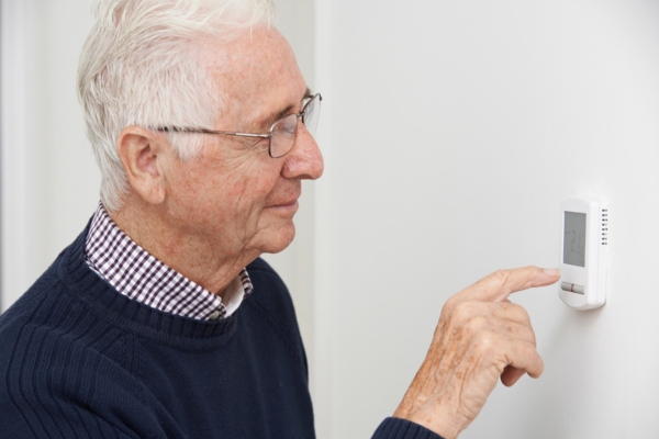 senior man adjusting home thermostat to reduce fuel consumption