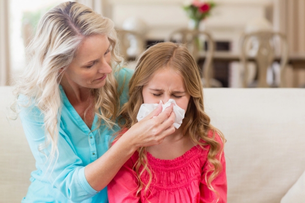 Mother helping her daughter blow her nose while on the sofa due to poor indoor air quality