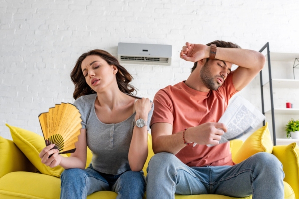 couple using hand fan and newspaper to keep cool depicting air conditioning emergency