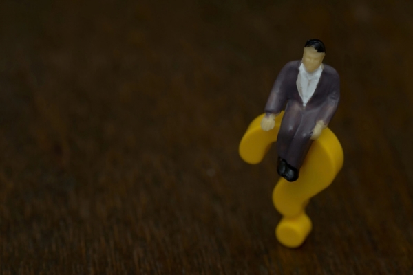 mini figurine of a man sitting on a yellow question mark depicting FAQs About Smart Thermostat vs Programmable Thermostat